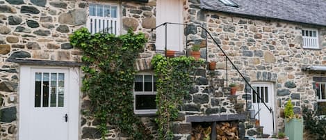 A stone building with a white door, windows, and a small porch area with a fire pit and potted plants.
