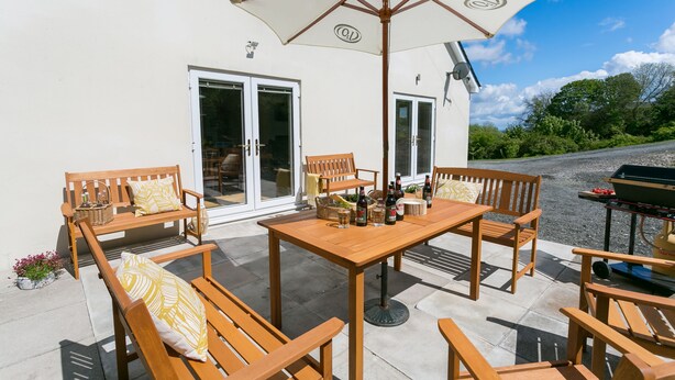 Una veranda esterna con mobili in legno, un tavolo e un barbecue.