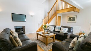 A living room with a fireplace, a wooden staircase, a sofa set, and a television mounted on the wall.