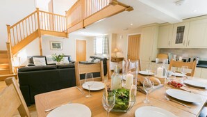 A dining area with a wooden table set for four, surrounded by chairs. A staircase with wooden railings is visible in the background.