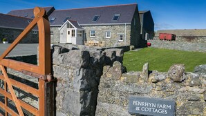 A stone cottage with a slate roof, a wooden gate, and a sign indicating 'Penrhyn Farm & Cottages'.
