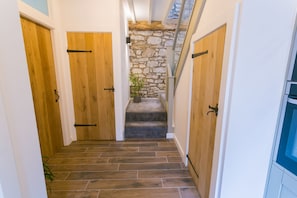 A narrow hallway with wooden doors, a stone wall, and a staircase leading to an upper level.