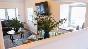 Un soggiorno moderno con un divano, un tavolo da pranzo con sedie, una TV a parete e ampie finestre.