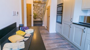 Una cucina con una scala in pietra, un piano di lavoro nero con formaggio e mobili bianchi.