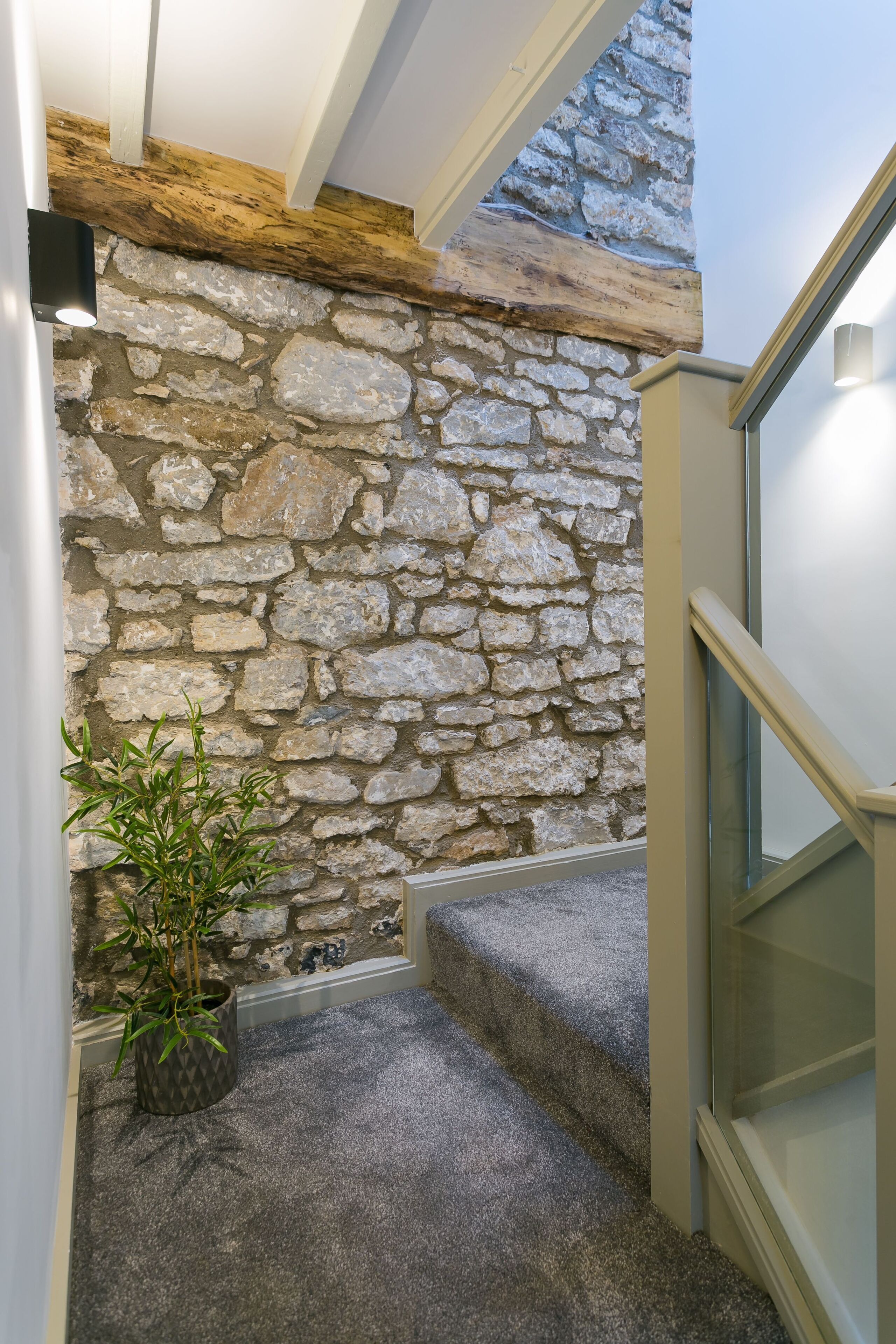A stone wall with a wooden beam, a potted plant, and a carpeted staircase.