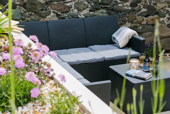 Relax in a serene outdoor seating area with a wicker sofa, small table, and lush greenery.