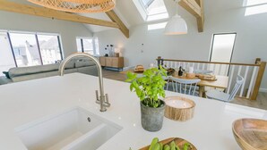 Cozinha moderna com ilha central, pia embutida e área de refeições com mesa e cadeiras de madeira.