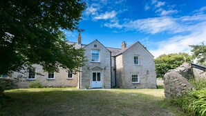 A two-story stone house with a central entrance, a small porch, and a grassy yard.
