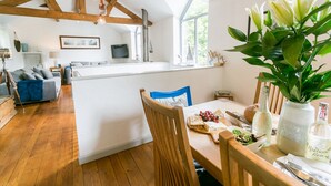 Een ruime woonkamer met een houten vloer, een gedekte eettafel en een keuken op de achtergrond.