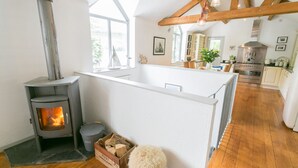 Een moderne keuken met een houtkachel, houten balken en uitzicht op de natuur.