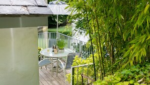 Een balkon met een glazen tafel en stoelen, omgeven door groen en uitzicht op een waterpartij.