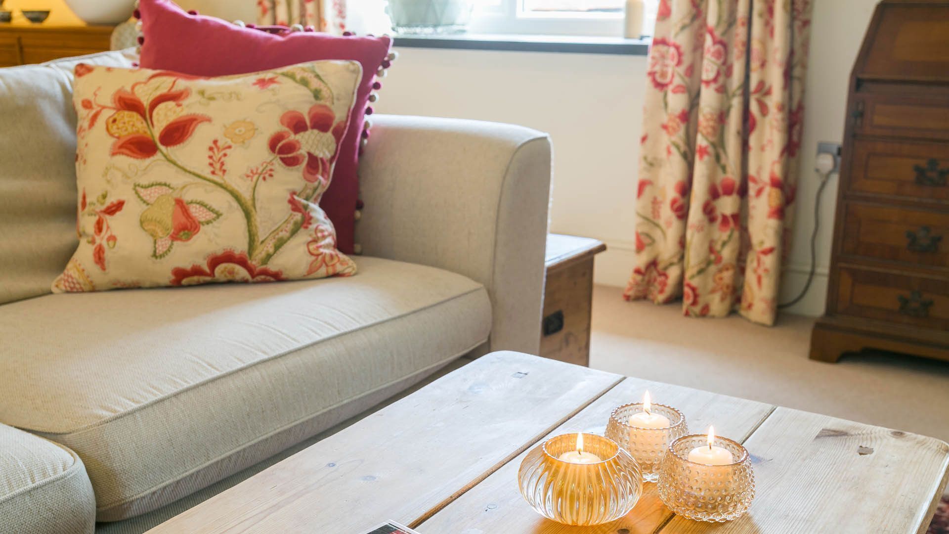 A cozy living room with a sofa, a wooden coffee table with candles, and floral curtains.