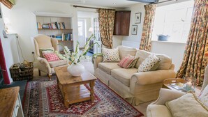 A cozy living room with a sofa, armchair, and a wooden coffee table. There is a bookshelf with books and a potted plant. - Ty Gwair -  a cosy fire that sleeps 4 guests  in 2 bedrooms (Pentraeth)