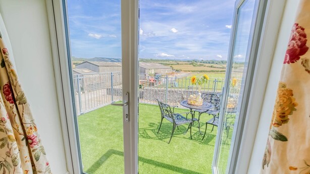 A balcony with a table and chairs, a grassy lawn, and a view of the countryside. - Ty Gwair -  a cosy fire that sleeps 4 guests  in 2 bedrooms (Pentraeth)