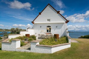Un edificio blanco con techo marrón, un pequeño porche con sillas y vista al mar.
