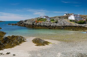 A coastal property with a white house, rocky shoreline, and clear blue water. - Pen y Graig -  an on the beach that sleeps 10 guests  in 5 bedrooms (Rhoscolyn)
