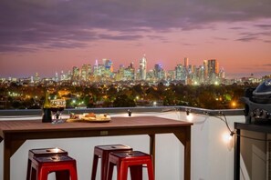 Eine Dachterrasse mit Blick auf den Stadtpanoramablick, ein Tisch mit einer Flasche und zwei rote Hocker.