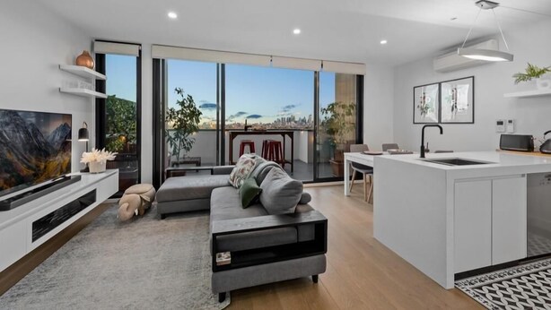 Ein modernes Wohnzimmer mit grauem Sofa, einem Flachbildfernseher und einem großen Fenster mit Blick auf die Stadt.