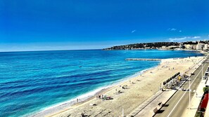 Una carretera costera con una playa a la derecha, mar azul cristalino y edificios al fondo.