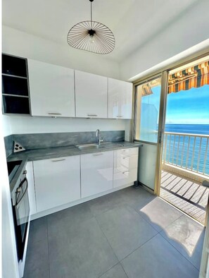 Una cocina moderna con armarios blancos, encimera gris y vistas al mar a través de un ventanal corredero.