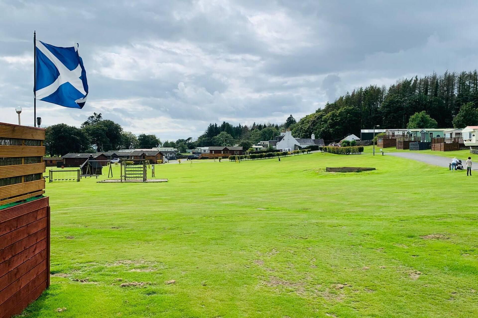 A grassy field with a flagpole and a flag, surrounded by buildings and trees.