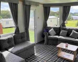 A living room with grey sofas, a coffee table, and a view of a green landscape through large windows. - Stunning 2-bed Apartment in Newton Stewart (Newton Stewart)