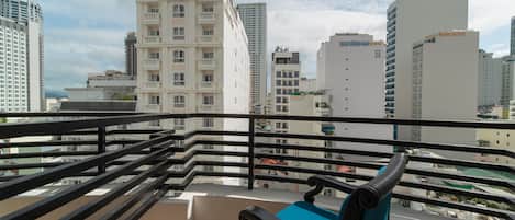 Varanda com cadeira azul e guarda-corrimão preto, com vista para um horizonte urbano de edifícios altos.