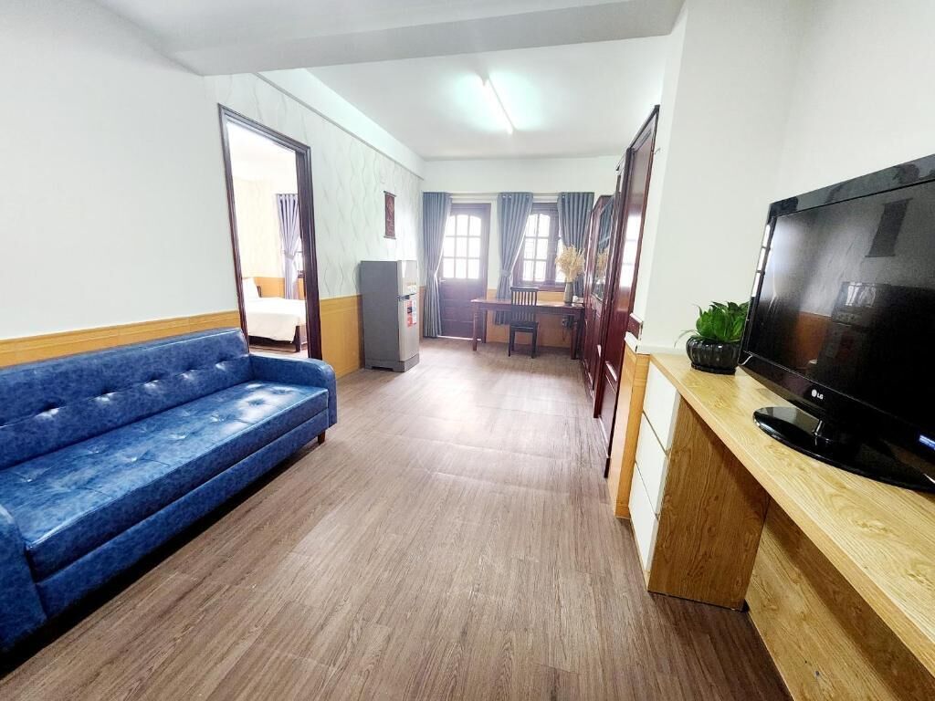 A room with a blue sofa, a wooden desk with a TV, and a dining area with a table and chairs.