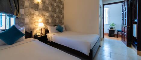 A hotel room with two beds, a wall-mounted lamp, a bedside table with a phone, and a view of the hallway.