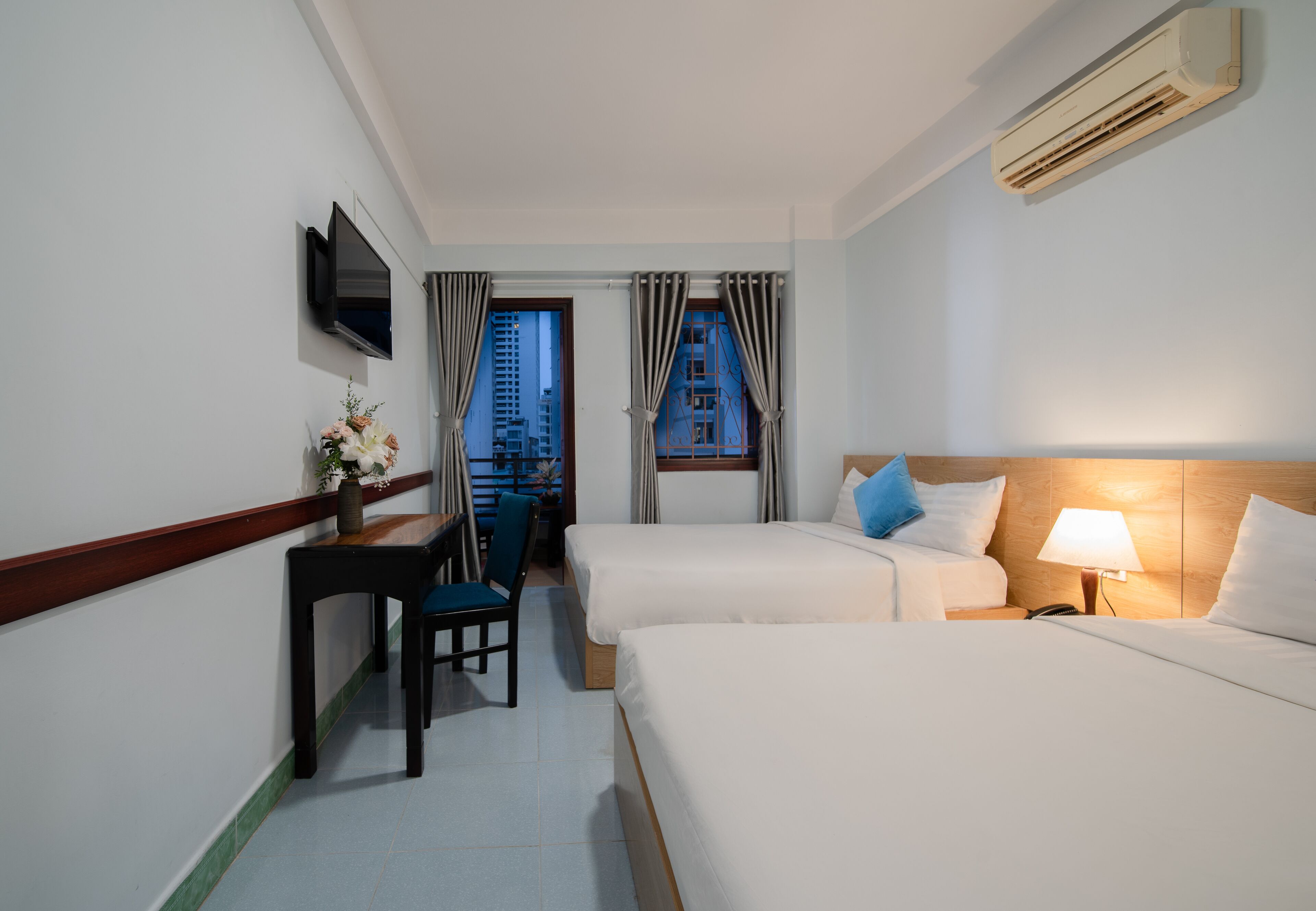 A hotel room with two beds, a desk, a chair, a TV, and a window with curtains.
