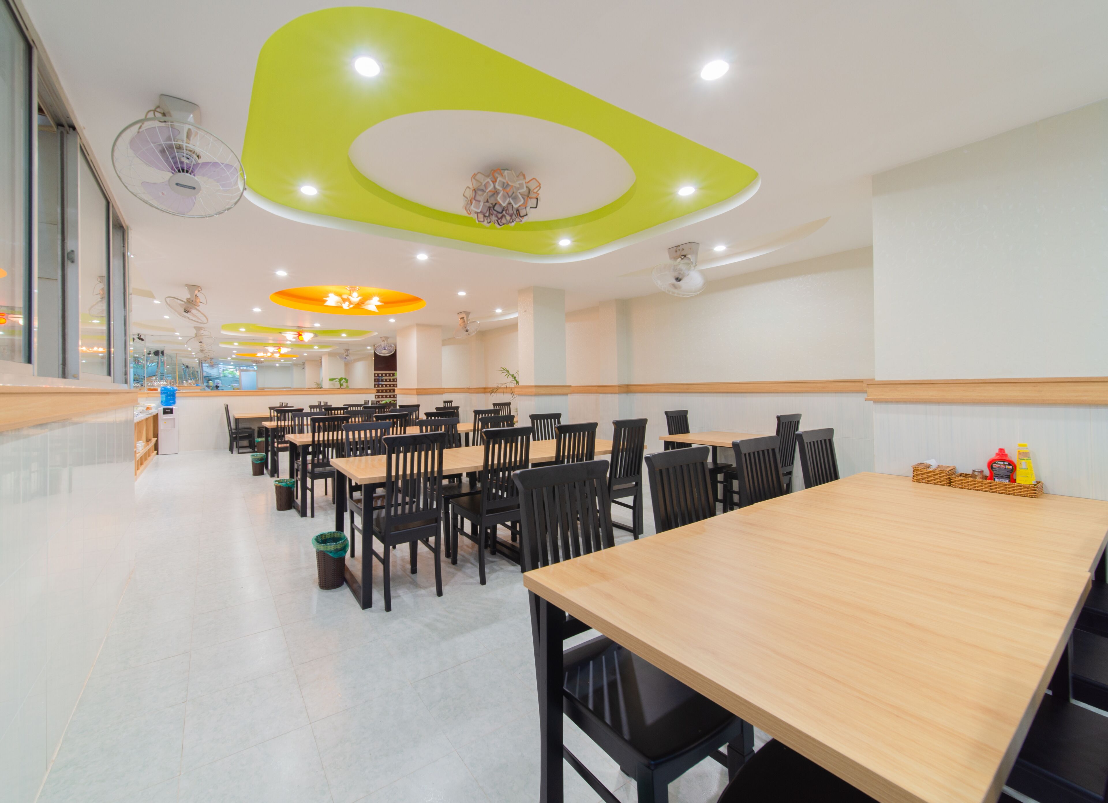A spacious cafeteria with multiple tables and chairs, a water dispenser, and a variety of seating arrangements.