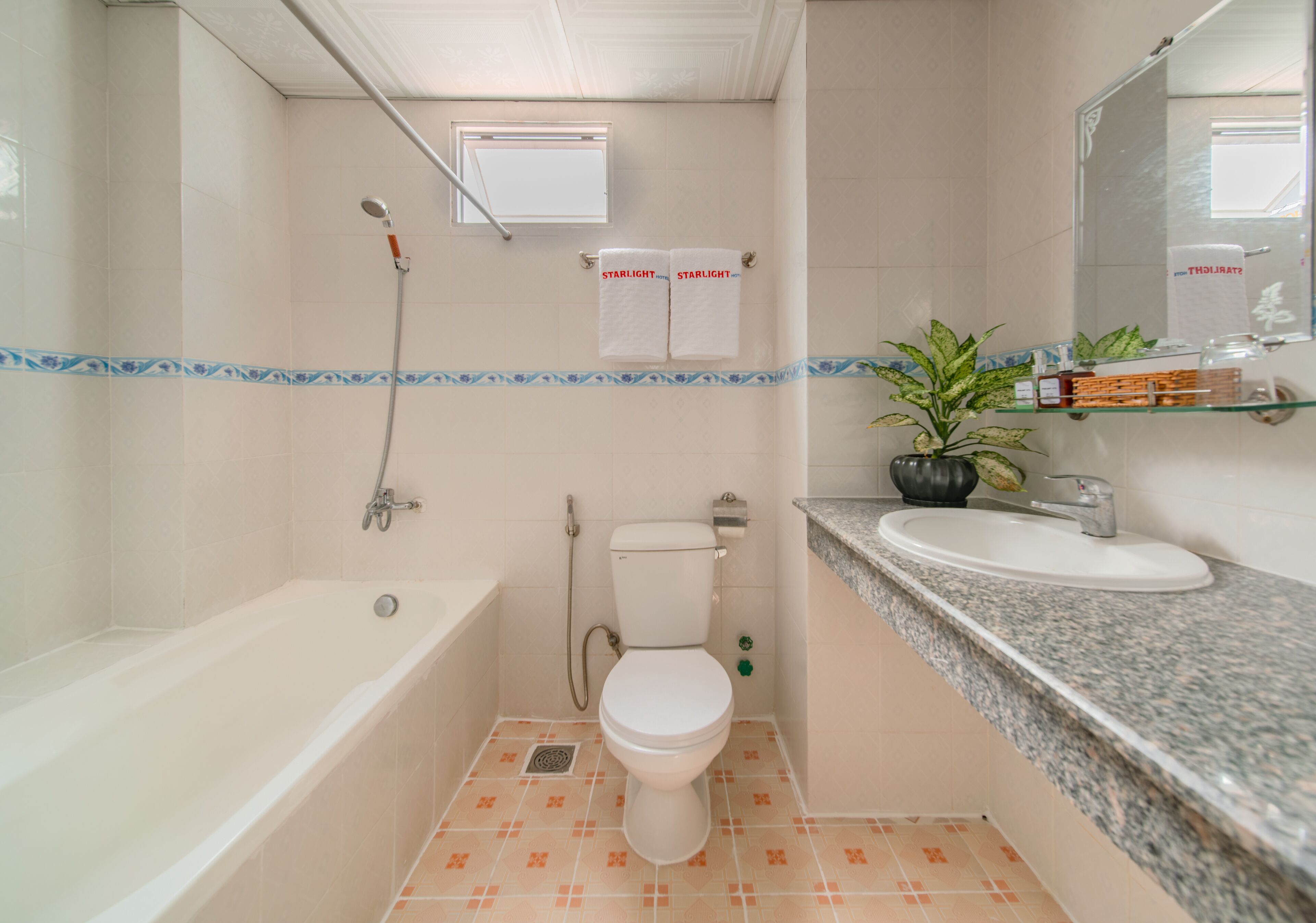 Et badeværelse med badekar, toilet og håndvask. Der hænger to håndklæder på væggen, og der står en plante på bordet.