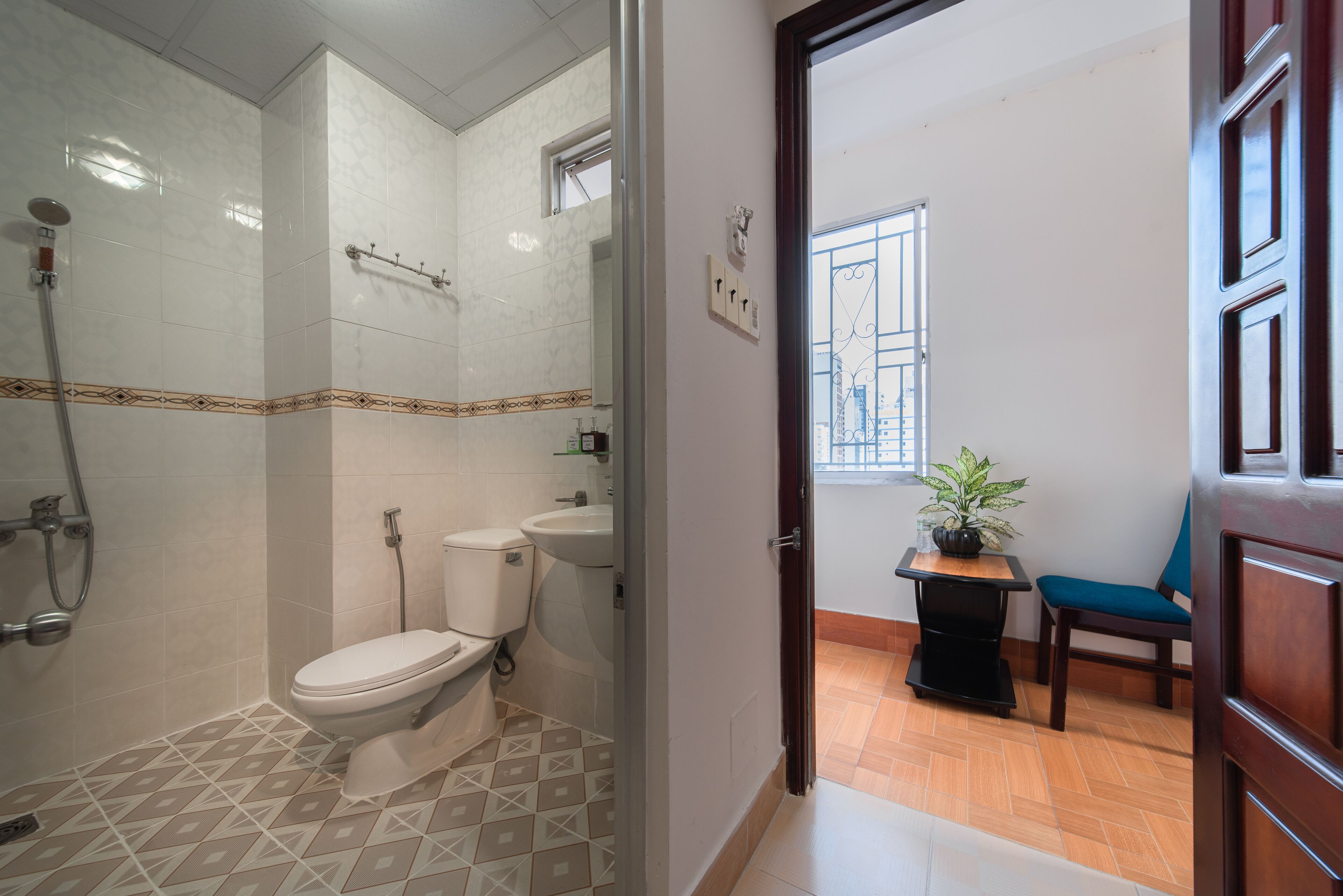 A bathroom with a shower, toilet, and sink, a potted plant, and a chair.