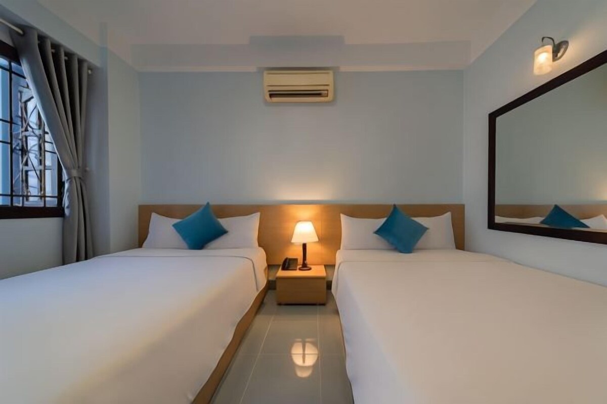 A hotel room with two beds, a nightstand with a lamp, an air conditioning unit, and a large mirror on the wall.