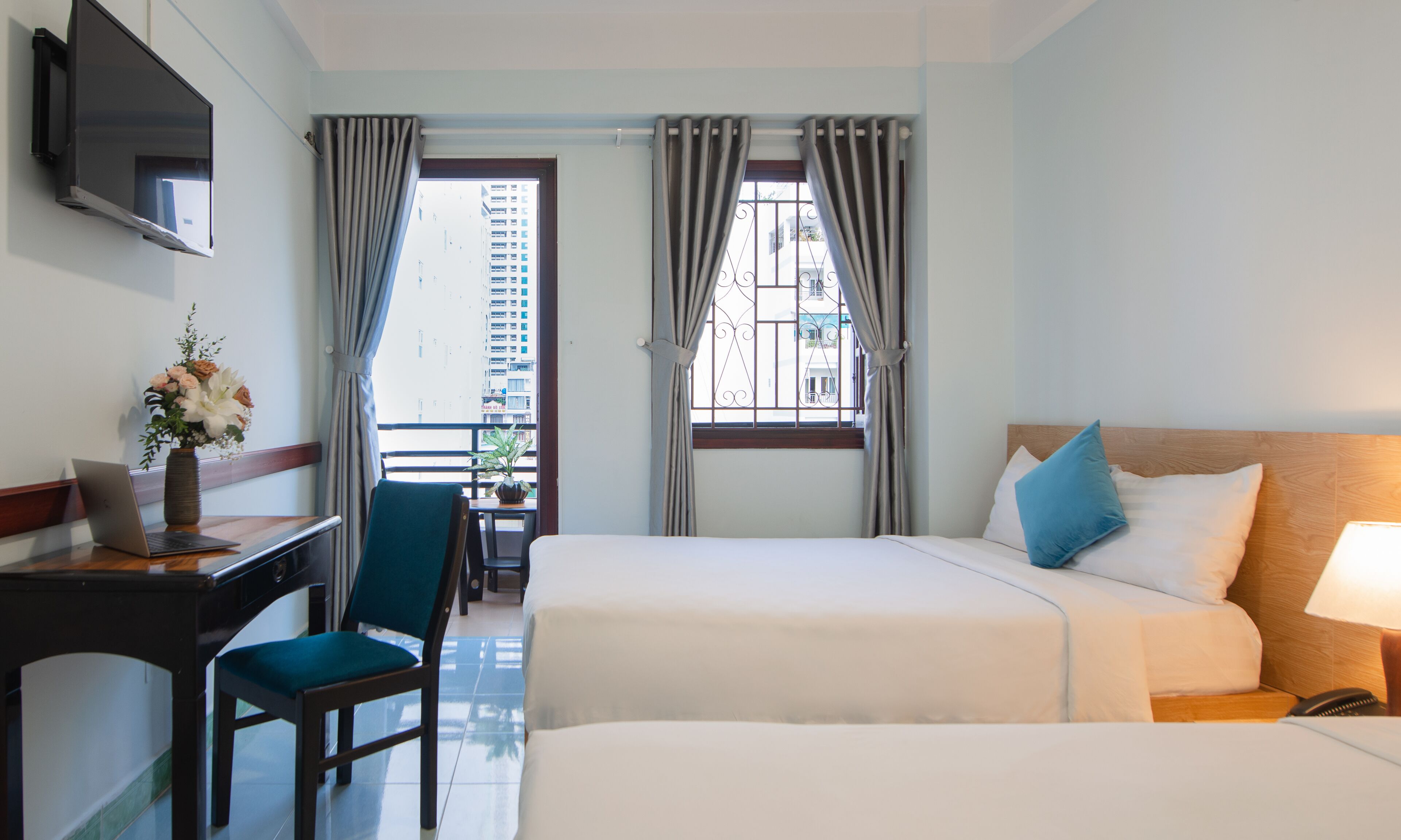 Habitación de hotel con cama, escritorio con una computadora portátil, una silla y ventana con cortinas.