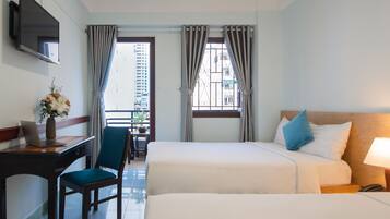 Habitación de hotel con cama, escritorio con una computadora portátil, una silla y ventana con cortinas.