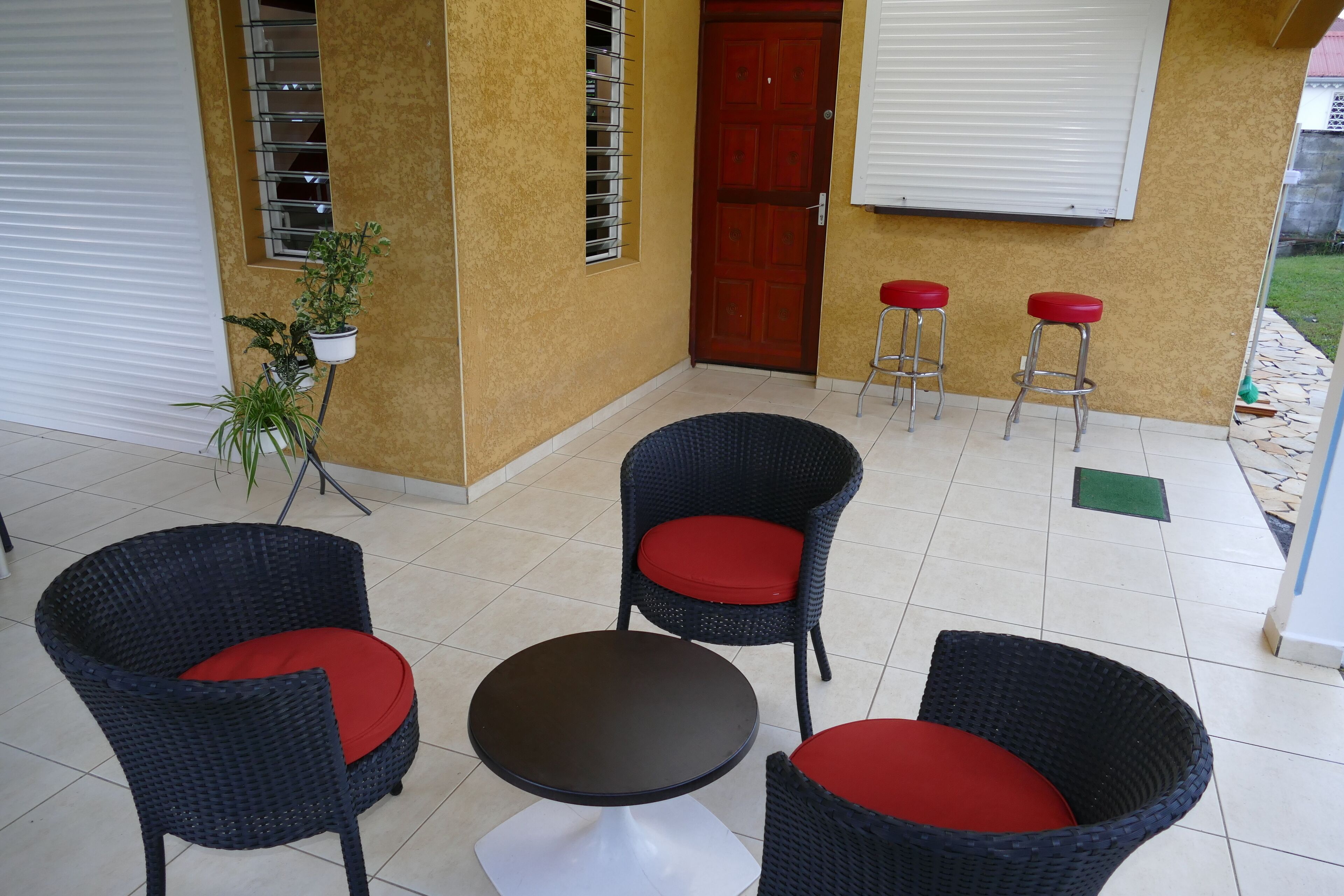 A patio area with wicker chairs and a table, a red door, and a potted plant.