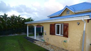 Une maison avec un toit bleu, un chemin de pierre et une terrasse aménagée avec du mobilier d’extérieur.