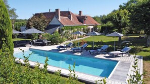 A swimming pool with lounge chairs and umbrellas, surrounded by a garden and a house.