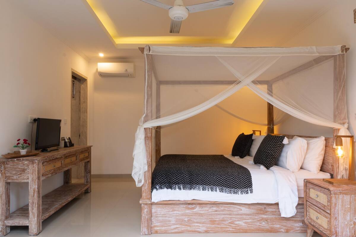A bedroom with a canopy bed, a wooden desk, and a television.