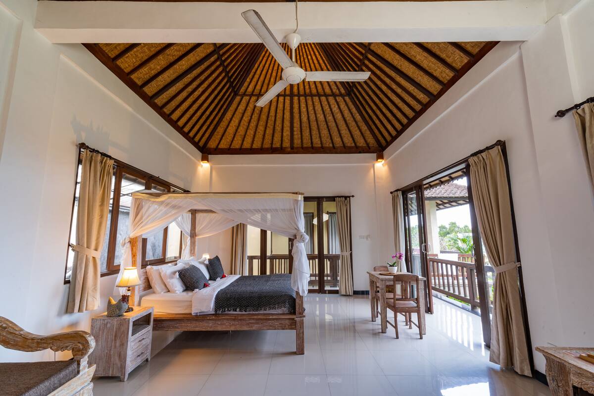 A spacious bedroom with a canopy bed, a ceiling fan, and a balcony with curtains.