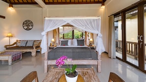 Une chambre à coucher avec un lit à baldaquin, un canapé, une table ornée d’une orchidée en pot et une vue sur l’extérieur.
