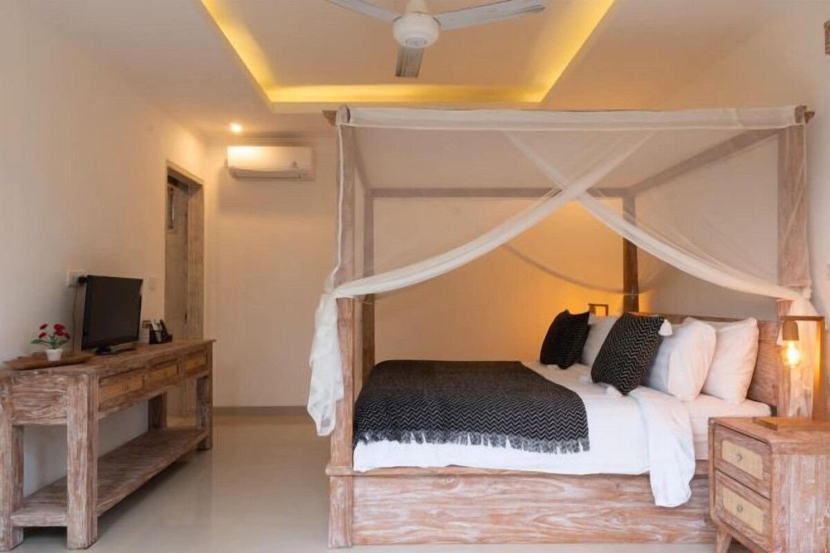 A bedroom with a canopy bed, a wooden desk, and a television.