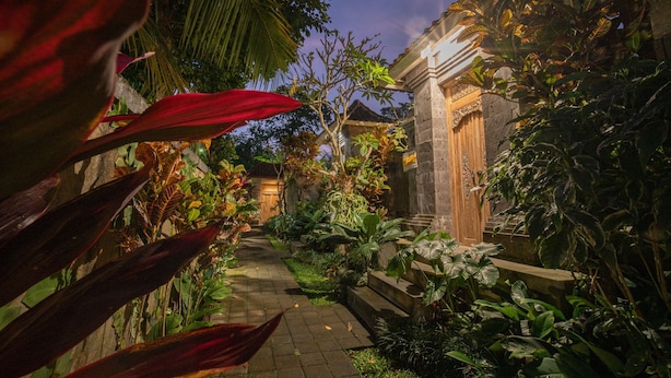 Un sentier de jardin mène à un bâtiment traditionnel doté d’un escalier en pierre et d’une porte en bois.