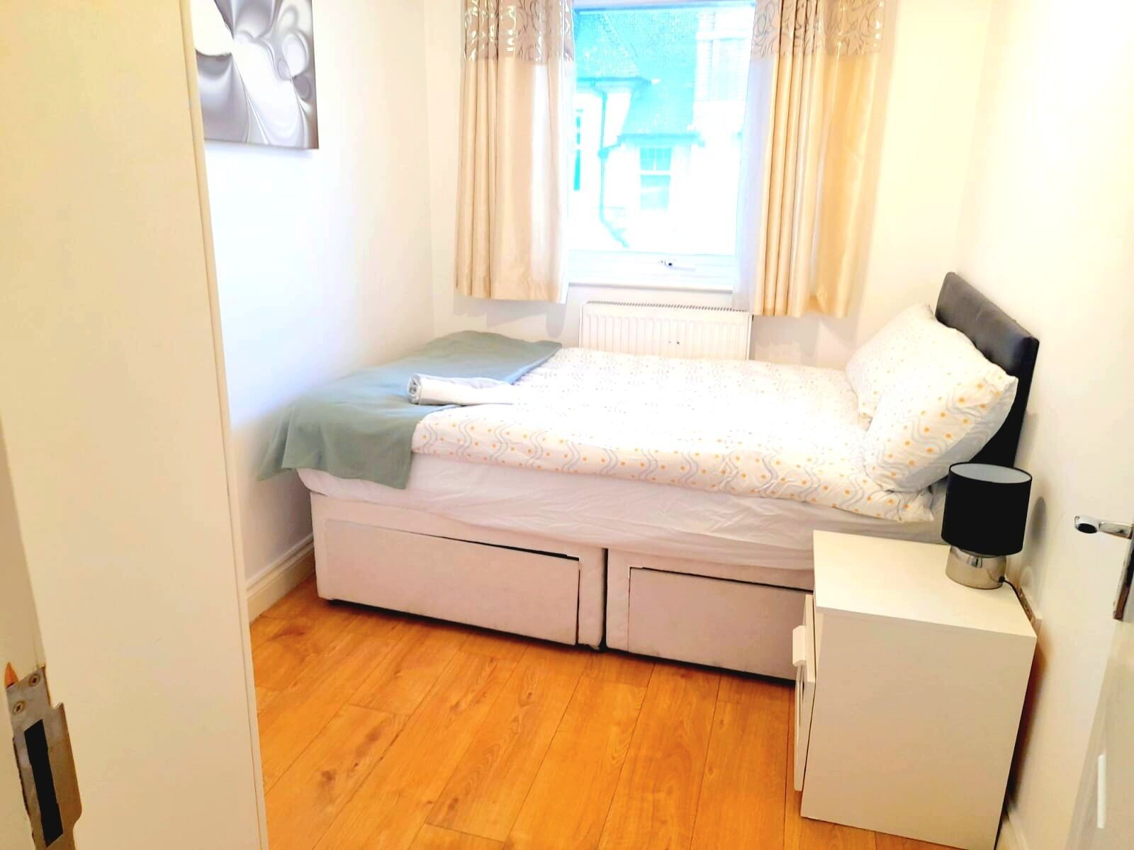 Un dormitorio con una cama, una mesita de noche, un radiador y una ventana con cortinas.