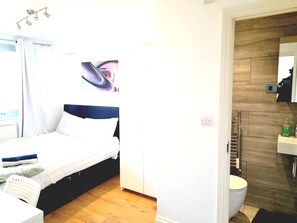 Une chambre à coucher comprenant un lit, une chaise, une table de chevet, ainsi qu’une salle de bain avec des toilettes et un lavabo.