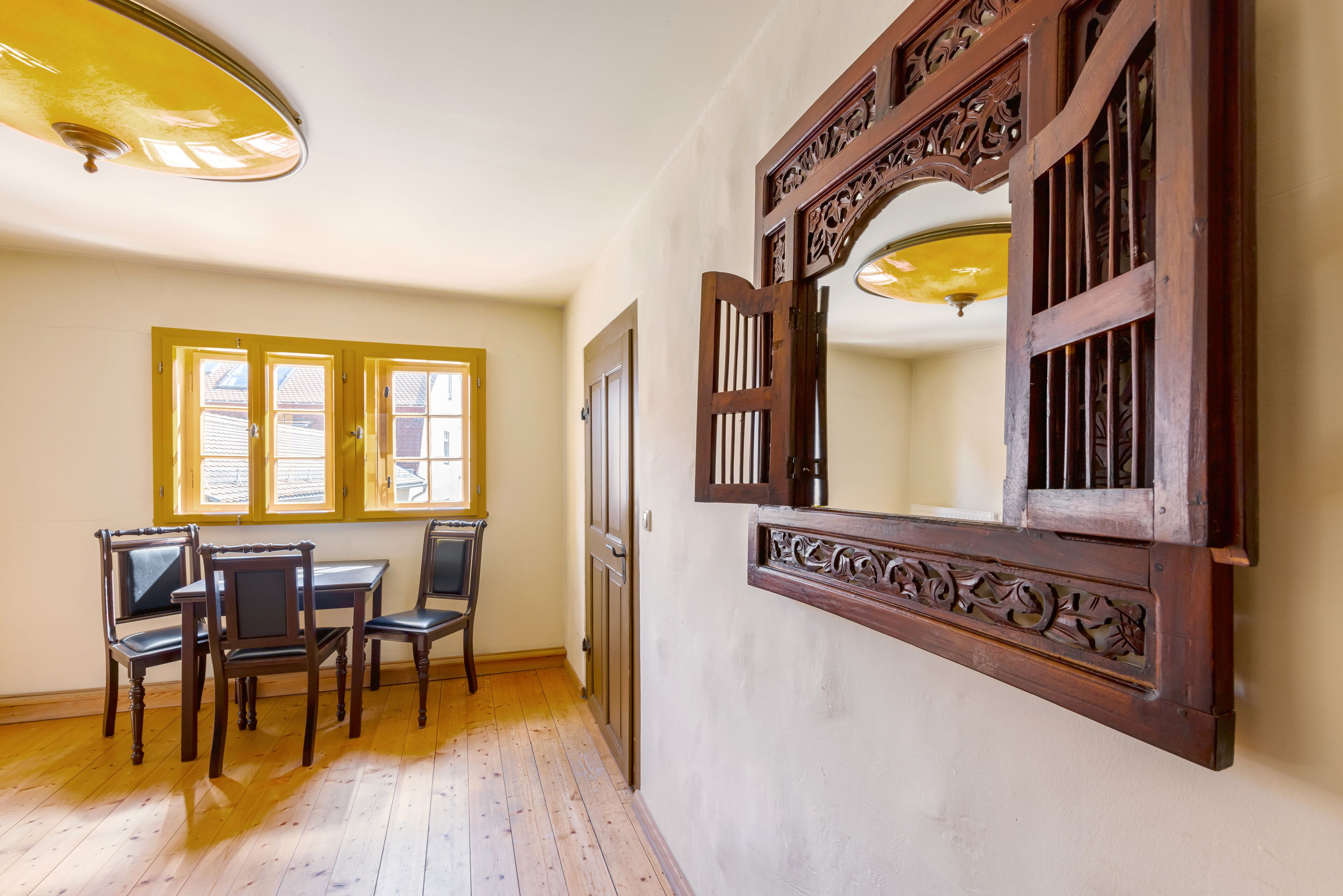 Una habitación con piso de madera, una mesa de comedor con sillas y un espejo grande con detalles de madera labrada.