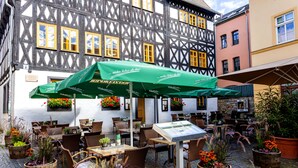 An outdoor café with tables and chairs, surrounded by potted plants and a traditional building with timber framing. - Watzdorfer Geleitschenke und Herberge (Weimar)
