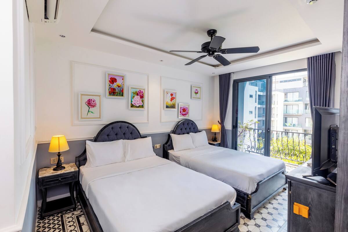 A hotel room with two beds, a ceiling fan, artwork on the wall, and a balcony with a view.