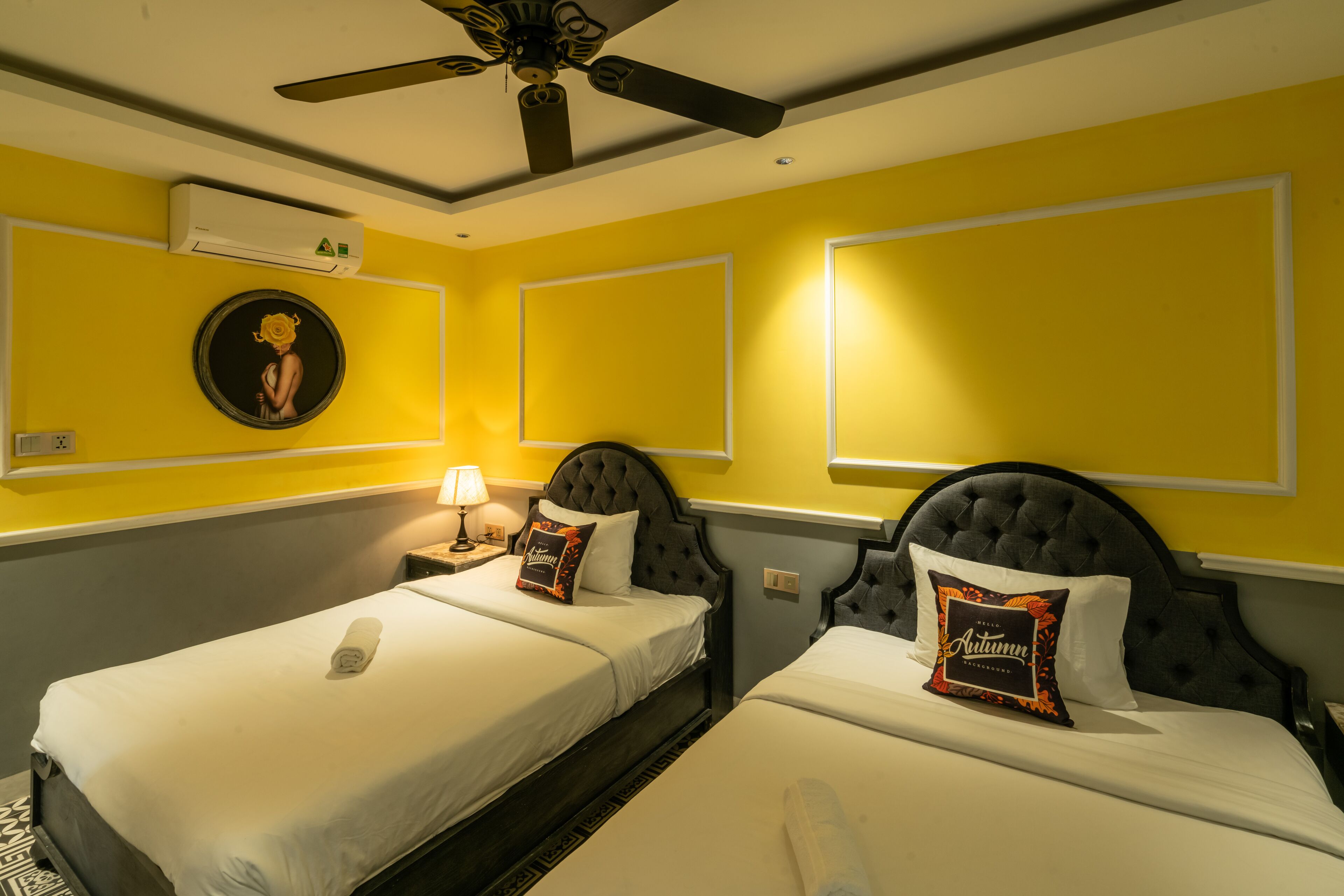 Une chambre d’hôtel avec deux lits, un ventilateur de plafond, un appareil de climatisation et un tableau encadré au mur.